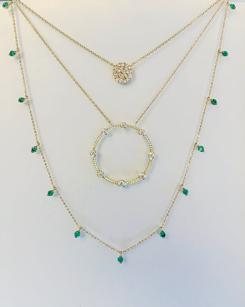 3 necklaces layered. yellow gold diamond pavé disk, 14k yellow gold diamond open negative space circle pendant, and 14k yellow gold emerald dangle drop necklace 