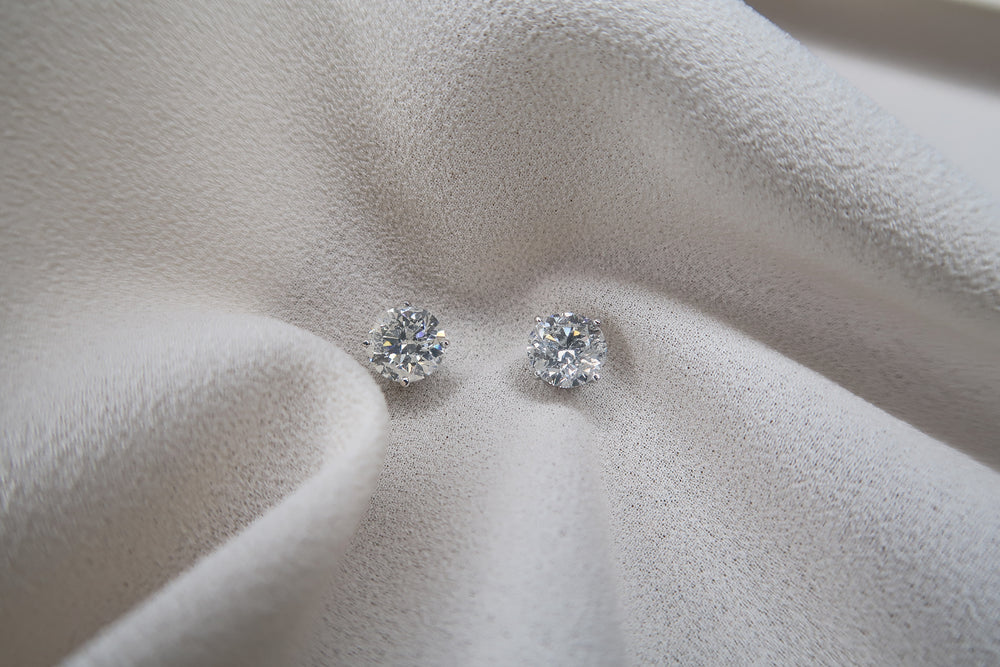 4 prong 14k white gold diamond earrings 2 carats sitting on a piece of white silk.. 